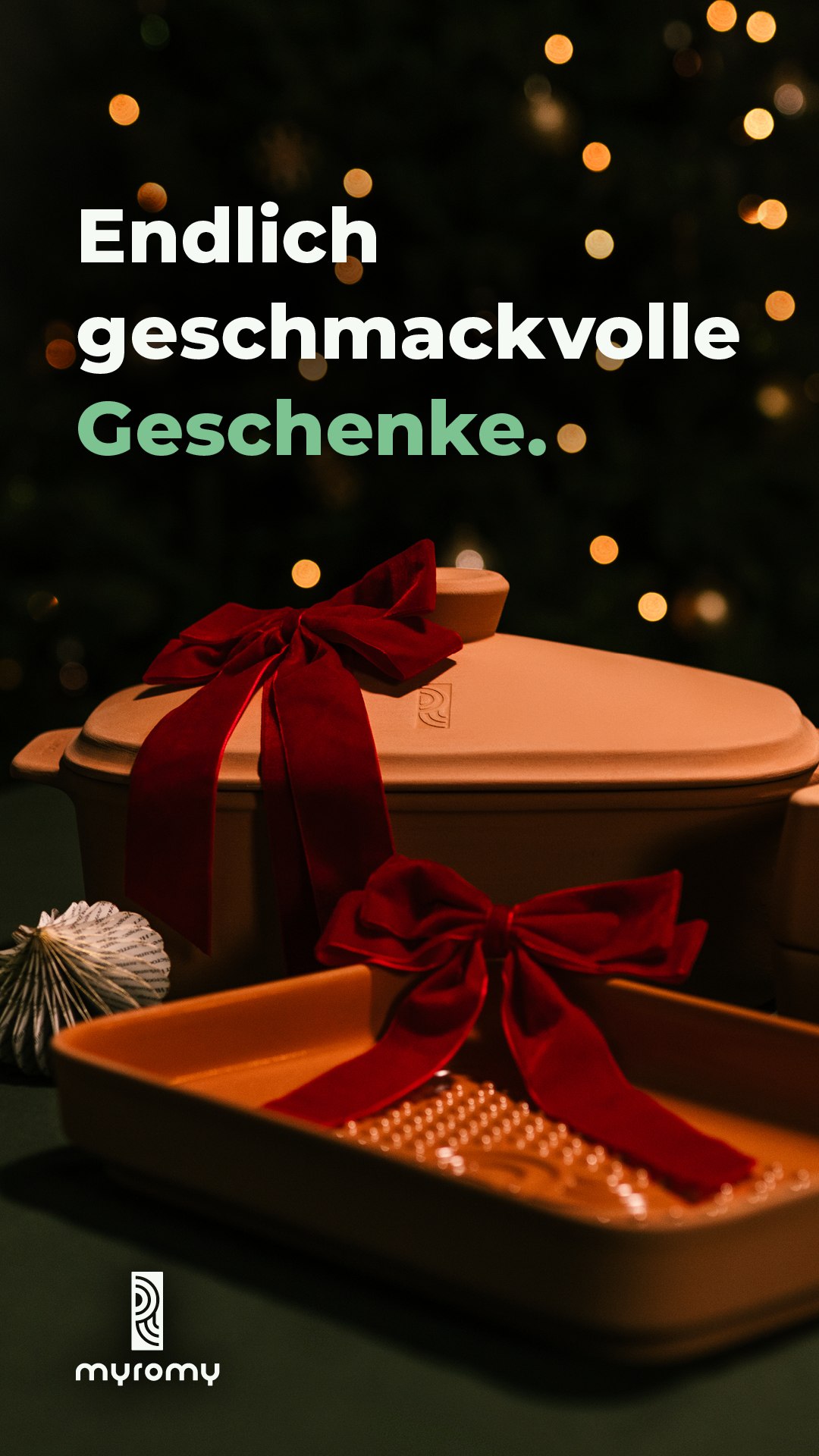 Ein Set aus hellbraunem Geschirr mit roten Samtschleifen steht auf einem Tisch mit festlichen Lichtern und einem Weihnachtsbaum im Hintergrund, perfekt für eine Event-Kampagne Tag der deutschen Einheit. Der deutsche Text lautet: Endlich geschmackvolle Geschenke.