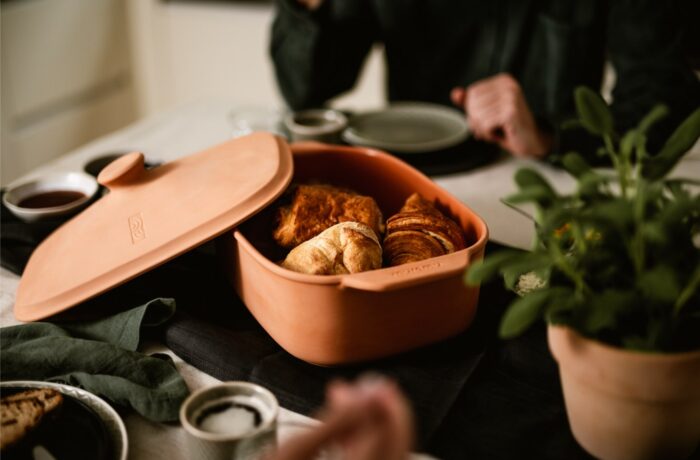 Eine Terrakottaschale mit Croissants und Gebäck steht auf einem Esstisch, umgeben von kleinen Schalen, Tellern und einer Topfpflanze - perfekt für eine Event-Kampagne zum Tag der deutschen Einheit, mit zwei Personen, die teilweise im Hintergrund zu sehen sind. Eine Terrakottaschale mit Croissants und Gebäck steht auf einem Esstisch, umgeben von kleinen Schalen, Tellern und einer Topfpflanze - perfekt für eine Event-Kampagne zum Tag der deutschen Einheit, mit zwei Personen, die teilweise im Hintergrund zu sehen sind.