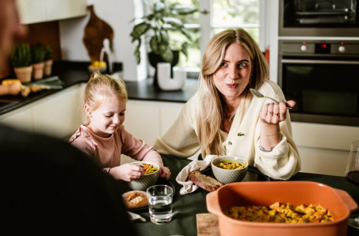 Eine Frau und ein junges Mädchen sitzen an einem Küchentisch, lächeln und essen gemeinsam. Während das Sonnenlicht die Küche für die Event-Kampagne Tag der deutschen Einheit erfüllt, bilden die Pflanzen am Fenster einen hellen Hintergrund für ihre Feier. Eine Frau und ein junges Mädchen sitzen an einem Küchentisch, lächeln und essen gemeinsam. Während das Sonnenlicht die Küche für die Event-Kampagne Tag der deutschen Einheit erfüllt, bilden die Pflanzen am Fenster einen hellen Hintergrund für ihre Feier.